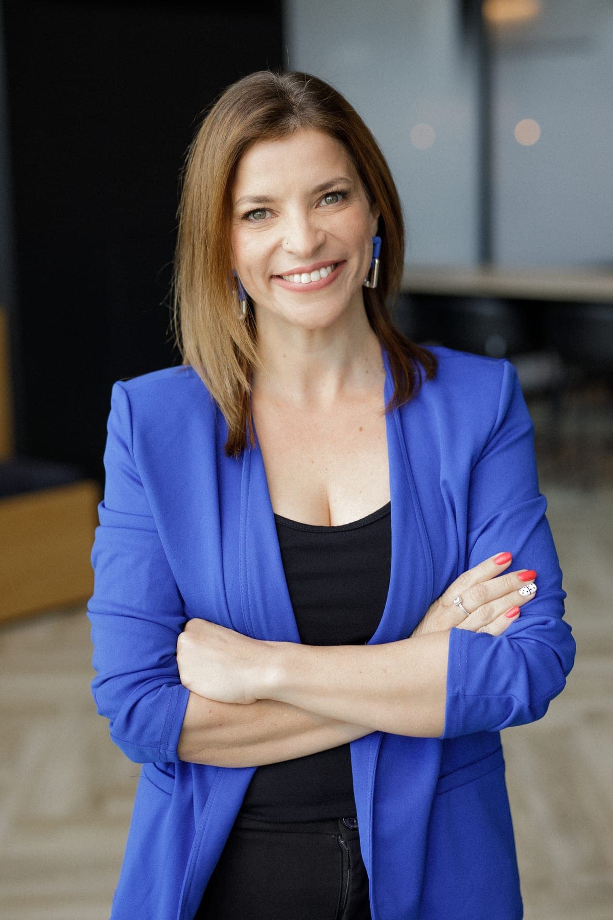 Ady Mor-Biran standing with arms crossed, smiling, in a bright office in a cobalt blazer.